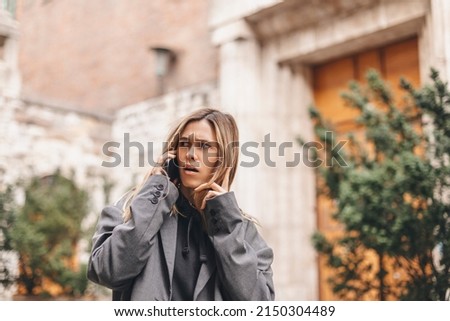 Upset woman. Woman talking sad by the bad news she hear on the cell mobile phone. Gloomy girl short hair wear grey suit and twisting a lock of hair on her finger. Royalty-Free Stock Photo #2150304489