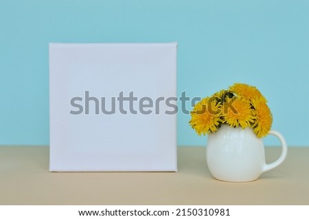 Dandelion bouquet in a vase and picture frame with copy space for mockup on a blue background.