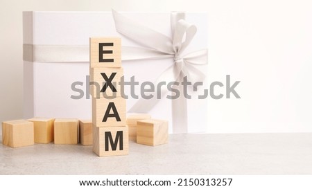 the Exam text is laid out in a pyramid of wooden cubes. in the background is a paper gift box with a shiny white ribbon