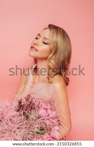 A sweet charming woman with flowers in a pink dress on a pink background smiles, happiness and luck