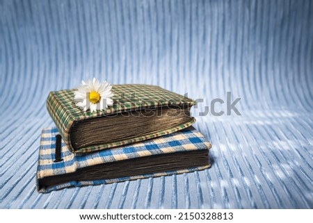 Old nostalgic photo album with small daisy flower on blue rippled background (copy space) - Books of Precious Memories