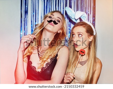 Were the life of the party. Shot of two beautiful young women having fun with props in a photobooth. Royalty-Free Stock Photo #2150332459
