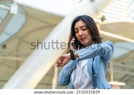 Confidence Asian businesswoman checking time on hand watch while walking in city street. Business woman working busy talking on mobile phone for online corporate business at office building district Royalty-Free Stock Photo #2150335839