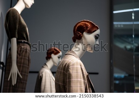 Fashion mannequins at storefront window in shopping mall. Midseason sale at style clothes retailer. Discount designer apparel displayed in shop or boutique.