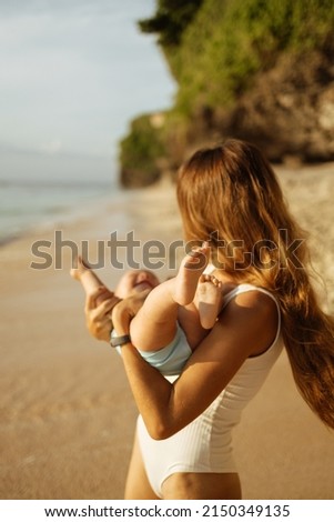Happy young mother play with her little baby daughter on the beach, hugs and kiss. Focus on baby feets
