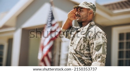 Patriotic young soldier saluting while standing outside his home. Member of the United States Marine Corps showing honour and respect on Veterans Day. Royalty-Free Stock Photo #2150353737