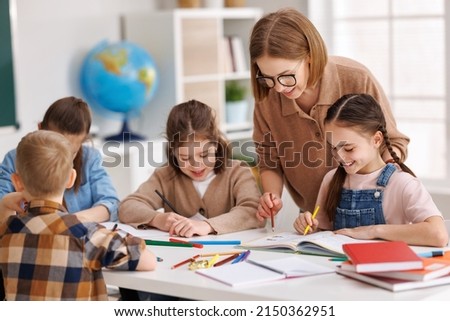 Smart woman teacher in casual clothes and glasses helping students to to schoolwork during lesson in light classroom at school Royalty-Free Stock Photo #2150362951
