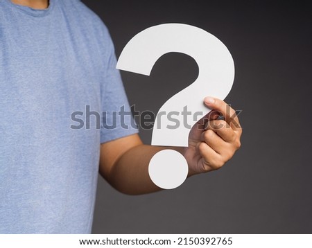 Question mark symbol concept. Hand holding a white question mark paper while standing on a gray background in the studio. Close-up photo. Space for text