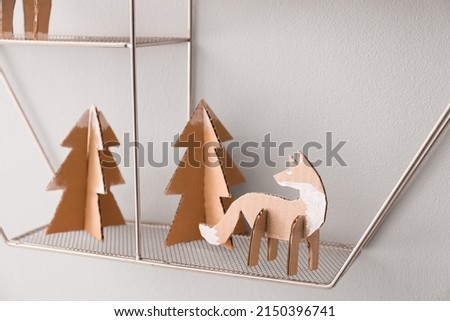 Handmade cardboard fox and fir trees on shelf near light wall