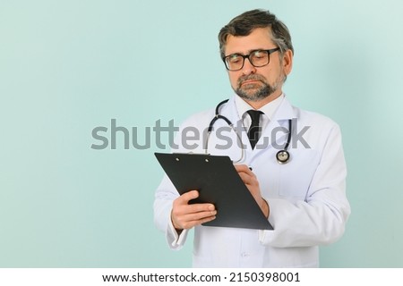 Senior doctor man wearing stethoscope and medical coat over blue background. Cheerful expression.