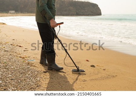 A man with a metal detector and a shovel on the seashore. A treasure hunter with a metal detector. A man is looking for a treasure. metal detector close-up. High quality photo