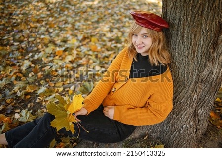 Smiling blonde teen girl with curly hair 15-16 year old posing outdoors over autumn nature background. Looking at camera.
