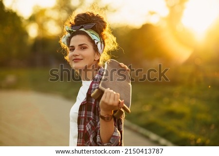 Portrait of beautiful caucasian woman holding skateboard in her hands standing outside.