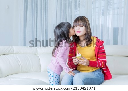 Cute little girl kissing her mother while giving a cupcake to celebrating mothers day in the living room