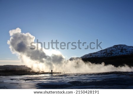 The silhouette of a tourist surrounded by the steam of a geyser that just erupted in the Geysir Park during a sunny winter day in Iceland, Europe