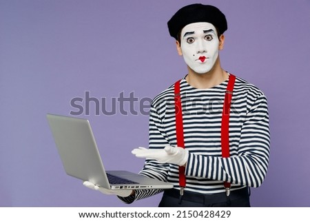 Charismatic surprised fun young mime man with white face mask wears striped shirt beret hold use work point hand on laptop pc computer isolated on plain pastel light violet background studio portrait