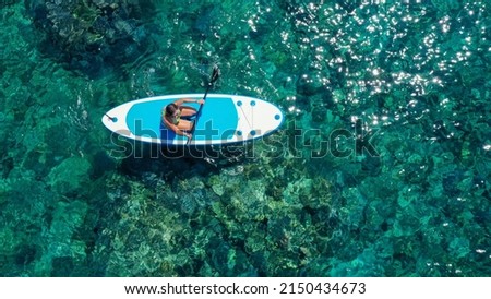 Top down view picture of a woman paddling on her knees on the sup board.