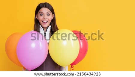 amazed kid with party colorful balloons on yellow background