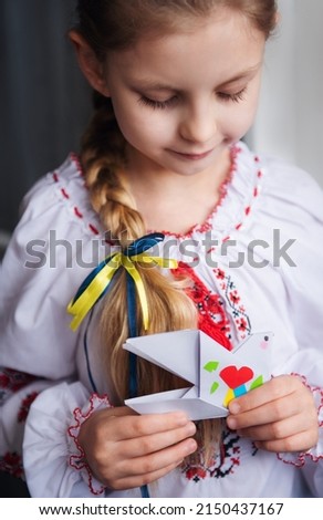 A little Ukrainian girl in traditional clothes holds a paper dove of peace in her hands. Support for Ukraine. Stop the war.