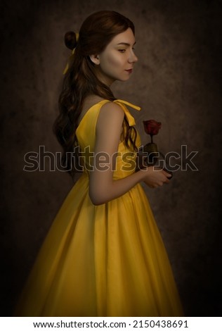 Pretty woman in the yellow long dress closeup with red rose in her hands. Beauty and the beast cosplay