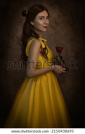 Pretty woman in the yellow long dress closeup with red rose in her hands. Beauty and the beast cosplay