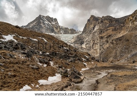A Barren Valley with Snowy Mountains in the Background and a glacier coming down from the peaks.