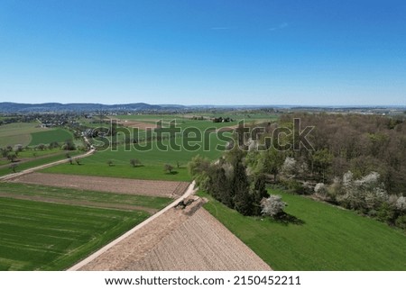 An aerial shot of greenery fields surrounded by trees in background of mountains in Germany