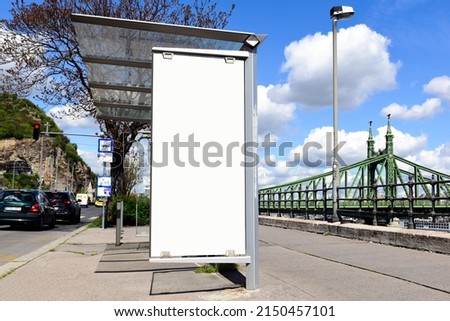 Bus shelter and bus stop on urban street in Europe. empty blank white ad space. old city street backgroind with steel suspension bridge. poster ad display. banner and copy space. base photo for mockup