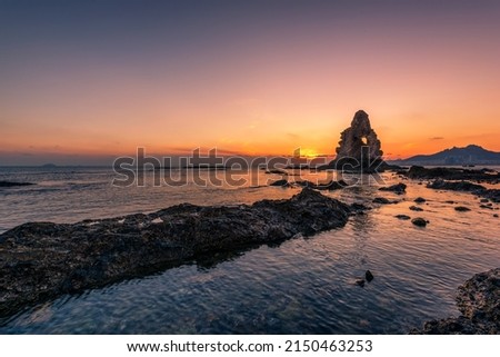 At sunset, strange looking rocks loom above the coast. Royalty-Free Stock Photo #2150463253