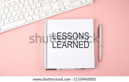 Pink office desk with keyboard and notebook with word LESSONS LEARNED,