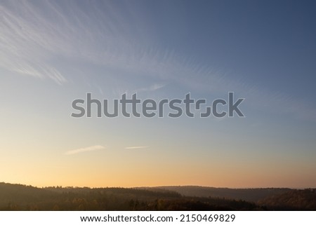 The sunset sky over the green hill with a forest and bushes
