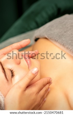 Beautiful young caucasian woman with closed eyes receiving a facial massage in a beauty salon