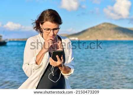 Happy 40s age woman in headphones with smartphone on the beach