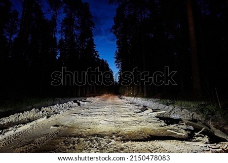 Night dirt road of planks and sand in the headlights against a dark gloomy sky. It is terrible and dangerous to go. Royalty-Free Stock Photo #2150478083