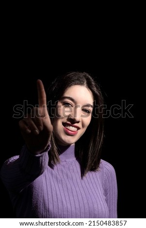 brunette woman showing the index finger on a black background pointing out that she is the best