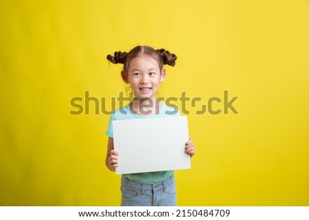 cute little schoolgirl girl holding a white sheet of paper on a yellow background