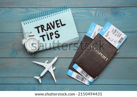 Notebook with phrase Travel Tips and tourist items on light blue wooden table, flat lay