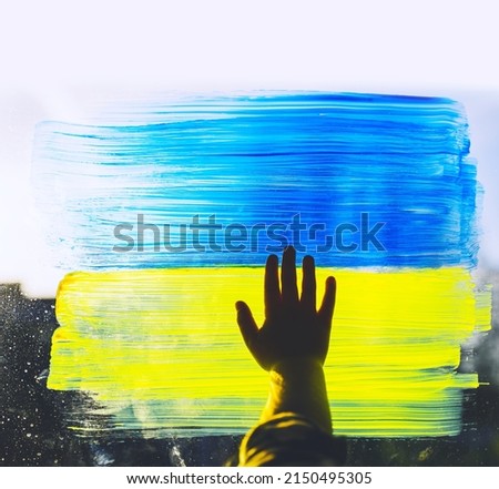 Child's hands touch painting yellow-blue flag of Ukraine on window. Hands of little kid on image of flag of Ukraine on glass. Support Ukrainians people and children. Concepts symbol, background.