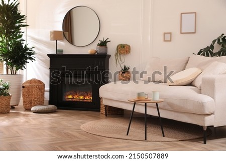 Stylish living room interior with electric fireplace, comfortable sofa and beautiful decor elements