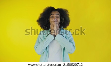 A young man with an Afro hairstyle on a yellow background is happy. Emotions on a colored background.