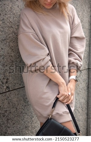 shopping leisure. closeup clothes design details. blonde girl in beige oversize dress stands casual with black bag in hands on the modern store background. lifestyle concept, free space
