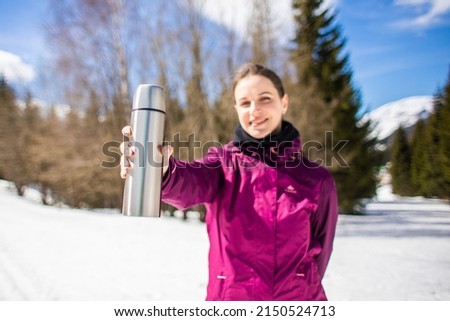 A young girl traveler is holding thermos against the background of mountains and snow. photo with focus on thermos