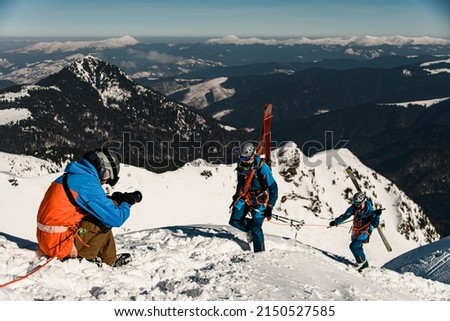 photographer takes pictures of male skiers with ski equipment climbing a snowy slope. Clear blue sky and winter mountain lanscape on background. Ski touring concept
