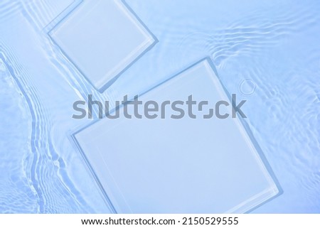 Two empty clear glass square podiums on blue transparent calm water texture with waves in sunlight. Abstract nature background for product presentation. Flat lay cosmetic mockup, copy space.