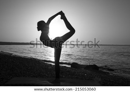 Woman stretching in yoga exercise fitness training at coastline at sunset, monochrome image