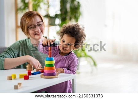 Mother looking at a child playing with an educational didactic toy. Preschool teacher with a child playing with didactic toys Royalty-Free Stock Photo #2150531373