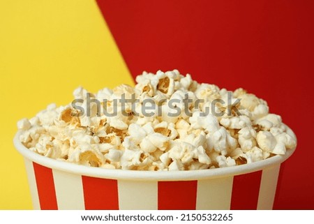 Striped paper cup with popcorn on two tone background.