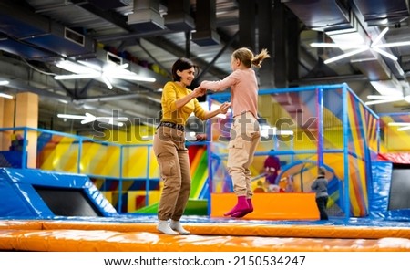 Pretty girl and her daughter kid jumping on colorful trampoline at playground park and smiling. Beautiful family during active entertaiments Royalty-Free Stock Photo #2150534247