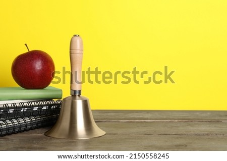 Golden school bell, apple and notebooks on wooden table against yellow background, space for text Royalty-Free Stock Photo #2150558245