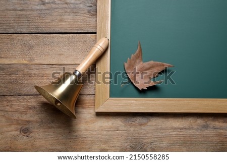 Golden school bell and green chalkboard with autumn leaf on wooden table, flat lay Royalty-Free Stock Photo #2150558285